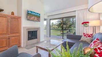 A spacious living room with a fireplace, a sofa set, and a large window offering a view of the outdoors.