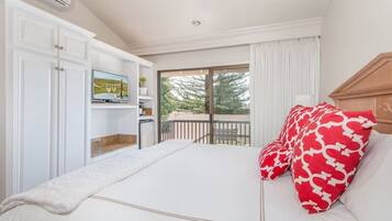 A hotel room with a bed, a TV, a small kitchenette, and a balcony with a view of trees.