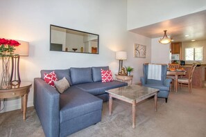 A living room with a sectional sofa, a coffee table, and a dining area with a table and chairs. - 2BR Near Wineries, Golf Course View, Parking (Napa)