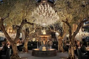 Un área de comedor al aire libre con una fuente central, rodeada de árboles e iluminada por candelabros.