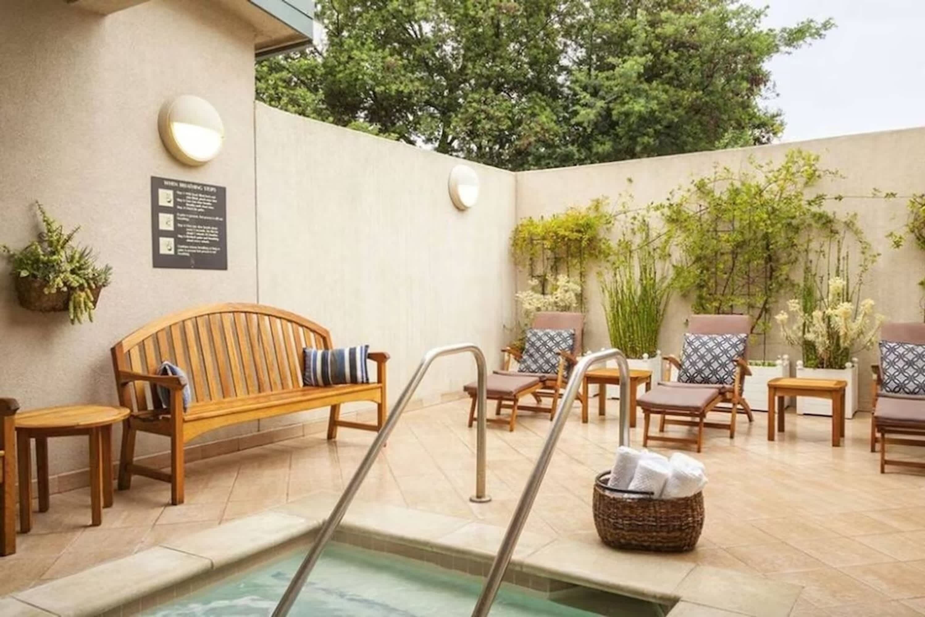 Un área junto a la piscina con un banco de madera, sillas de descanso y una mesita.