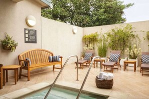 Un área junto a la piscina con un banco de madera, sillas de descanso y una mesita.