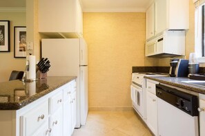 Una cocina con armarios blancos, encimera de granito, lavavajillas y cafetera.