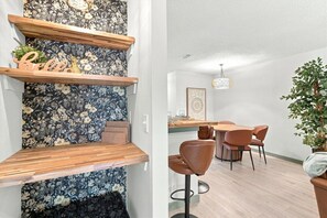 Thoughtfully styled built-in shelving with floral wallpaper brings character to the room, while the adjoining dining space adds warm wood tones, terracotta chairs, and woven lighting for a cozy, cohesive feel. - 2BR/2BA Home | Near The Domain & Apple (Austin)