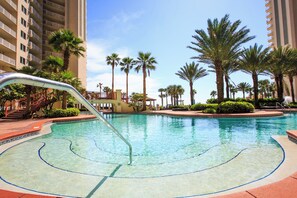 A swimming pool with a clear water feature, surrounded by palm trees and a multi-story building. - Shores of Panama 2327 (Panama City Beach)