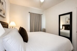 Habitación de hotel con una cama, una mesita de noche con lámpara, una ventana con cortinas y un espejo en la pared.