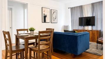Uma sala de estar com um sofá azul, mesa de jantar de madeira e cadeiras.