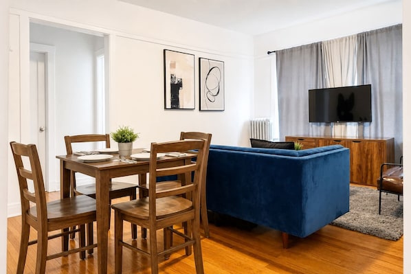 A living room with a blue sofa, wooden dining table, and chairs.