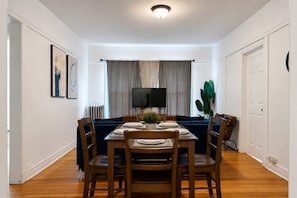 A dining area with a table set for four, a sofa, a television, and a plant.