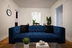 A living room with a blue sofa, a coffee table, a wall clock, and a potted plant.