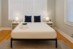 A neatly made bed with a white cover and two dark pillows, flanked by bedside tables with lamps and small plants. - Fully Set Up 3BR w/ Big Kitchen (Chicago)