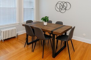 A dining area with a wooden table and black chairs, a potted plant, and a wall art piece. - Fully Set Up 3BR w/ Big Kitchen (Chicago)