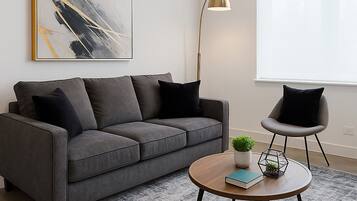 Un salon moderne avec un canapé gris, une table basse ronde, un lampadaire et un grand tableau abstrait accroché au mur.