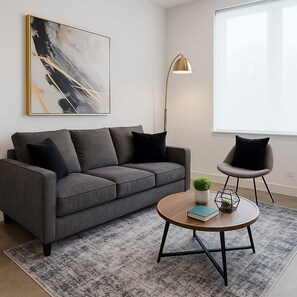 Un salon moderne avec un canapé gris, une table basse ronde, un lampadaire et un grand tableau abstrait accroché au mur.