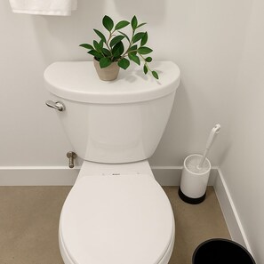 A white toilet with a plant on top, a toilet brush, and a bucket on the floor. - Stylish 4BR South Loop Home (Chicago)