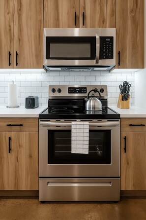 Une cuisine équipée d’appareils électroménagers en acier inoxydable, de meubles en bois, d’un crédence carrelée de carreaux blancs et d’une bouilloire posée sur la cuisinière.