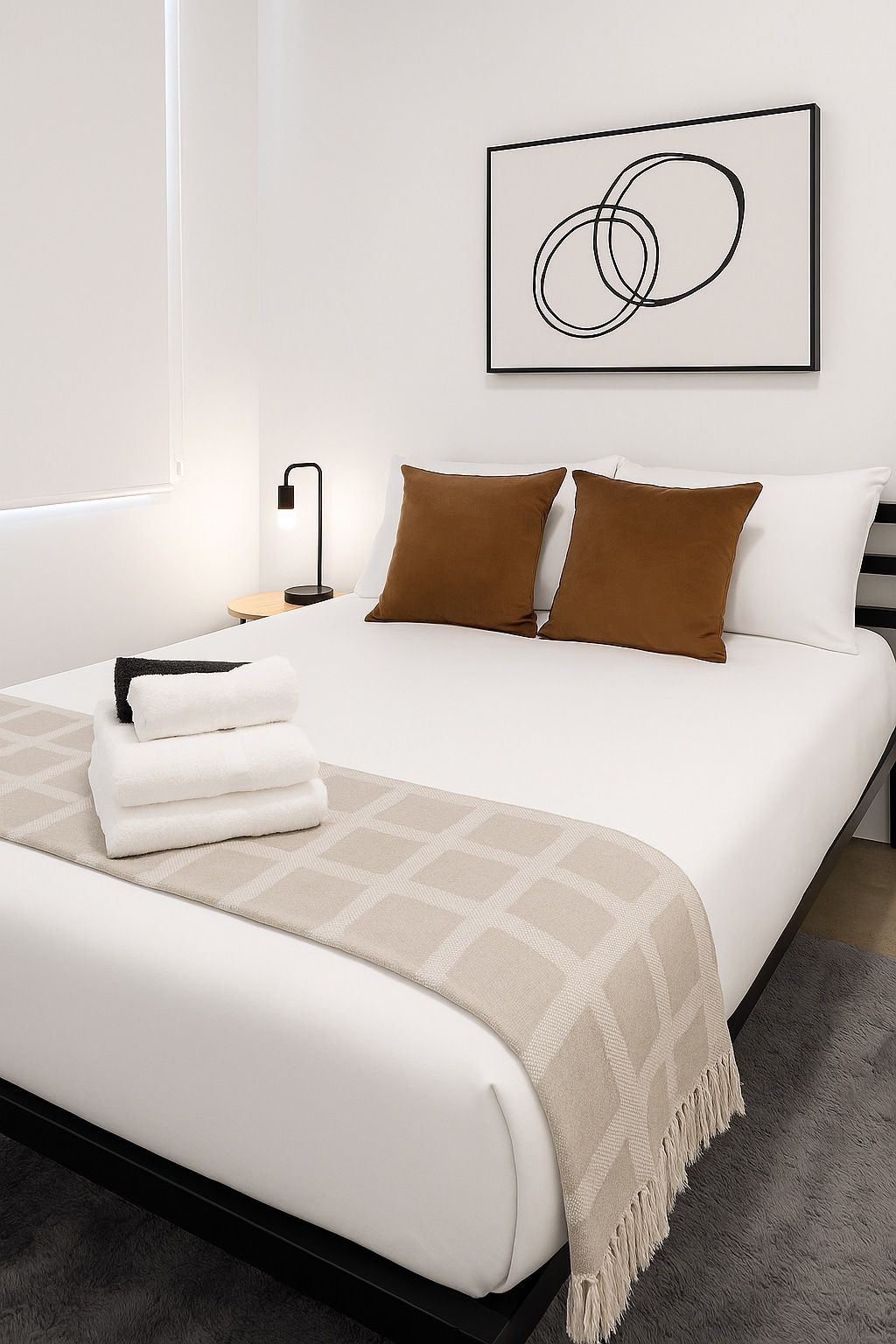 A modern bedroom with a large bed, a bedside table, a lamp, and a framed abstract artwork on the wall.