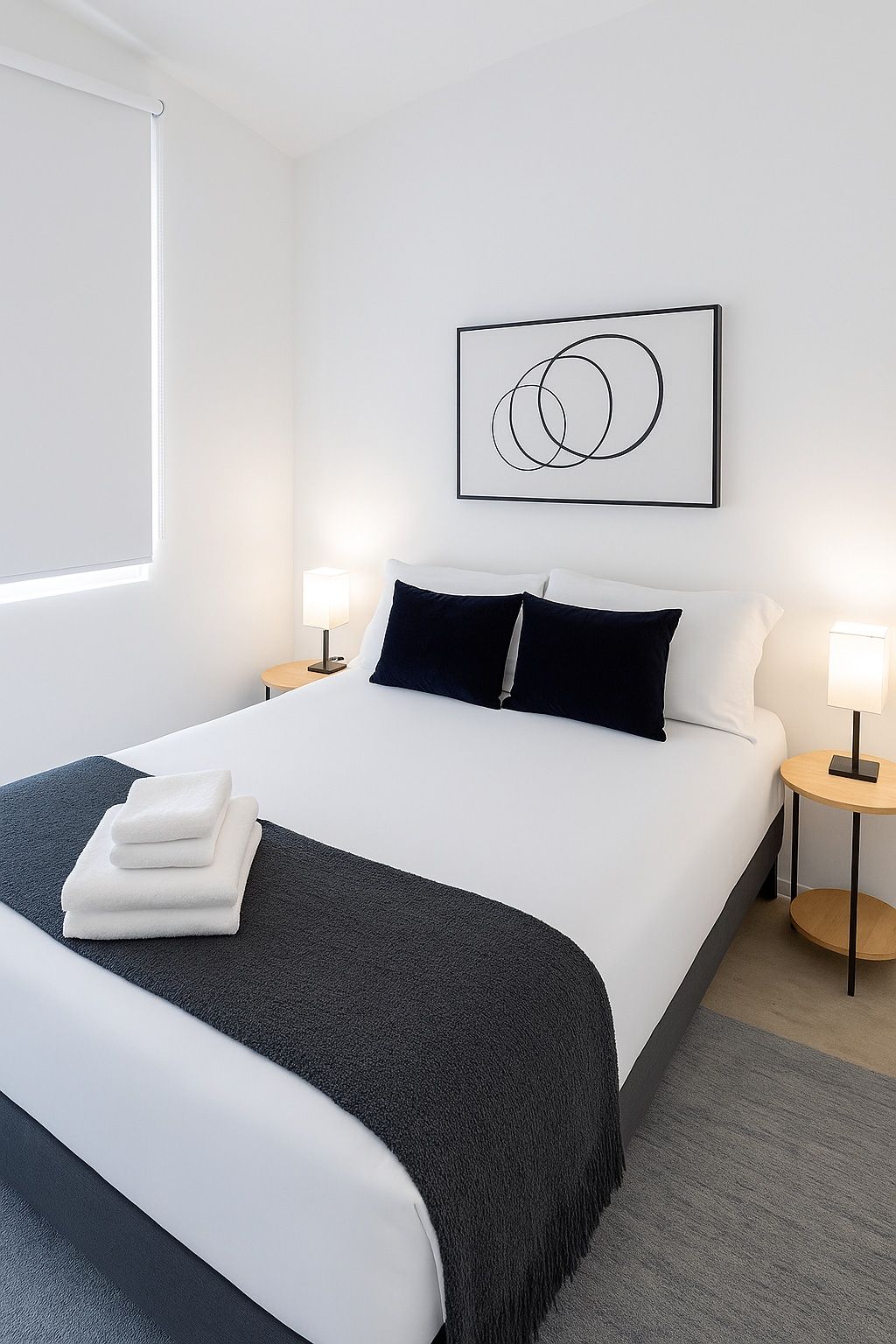 Ein Hotelzimmer mit einem ordentlich bezogenen Bett, einem Nachttisch mit Lampe, einem Wandbild und einem Fenster mit Jalousien.