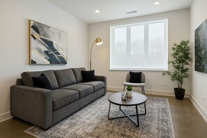 A modern living room with a gray sofa, a round coffee table, and a large window. - Stylish 4BR South Loop Home (Chicago)