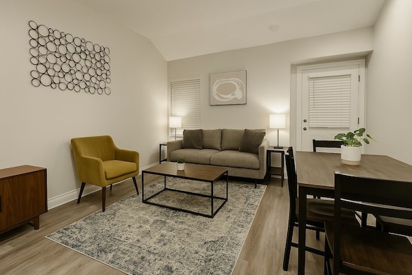 A living room with a sofa, armchair, coffee table, and a dining table with chairs. - 3BR Apt - Prime & Spacious (Chicago)