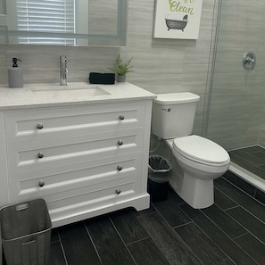 A modern bathroom with a white vanity, a toilet, and a shower area.
