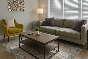 A living room with a sofa, armchair, coffee table, lamp, and wall decor. - 3BR Apt - Prime & Spacious (Chicago)