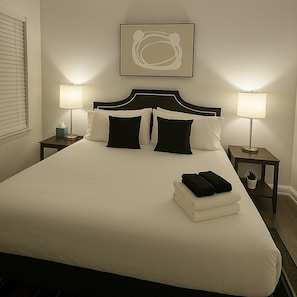 A neatly made bed with a white bedspread and black pillows, flanked by two bedside tables with lamps, one of which has a tissue box on it. - 3BR Apt - Prime & Spacious (Chicago)