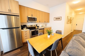 A compact kitchen with modern appliances, a dining table, and a sofa in a bright, minimalistic living area. - Stylish 4BR Stay-Prime Location (Chicago)