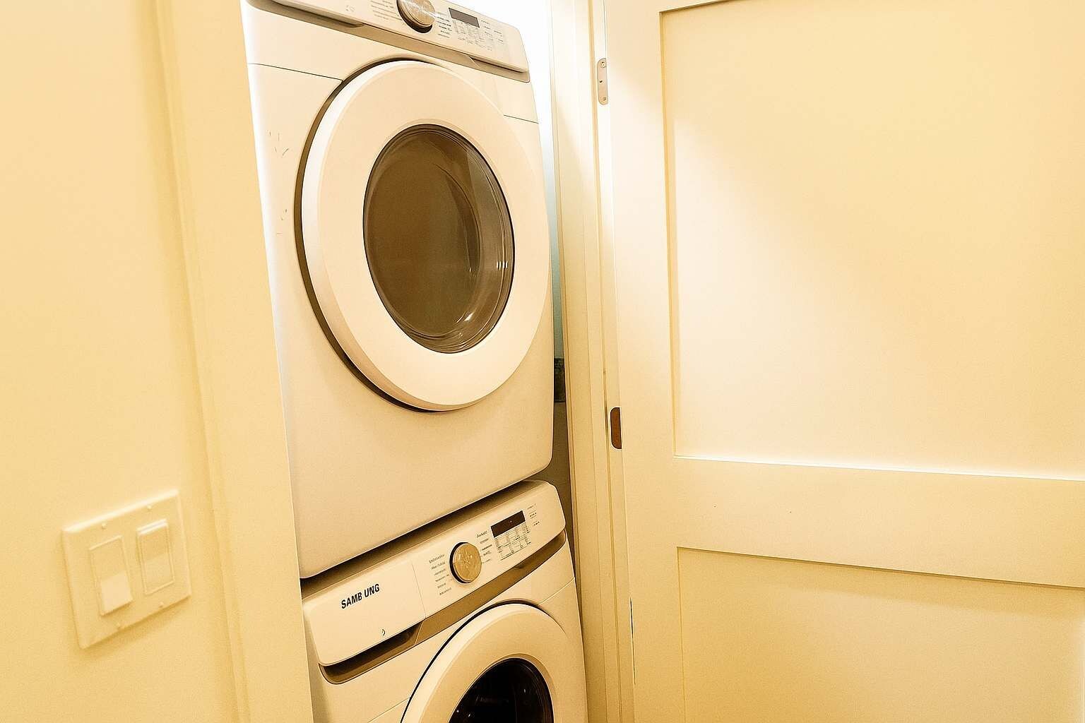 A stacked washer and dryer unit in a room with a plain door and a light switch on the wall.