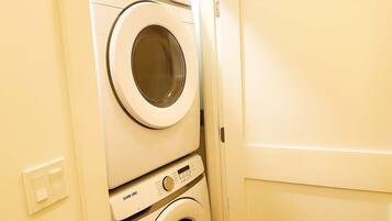 A stacked washer and dryer unit in a room with a plain door and a light switch on the wall.
