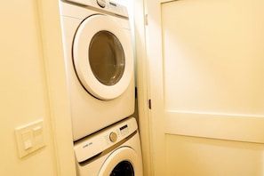 A stacked washer and dryer unit in a room with a plain door and a light switch on the wall. - Stylish 4BR Stay-Prime Location (Chicago)