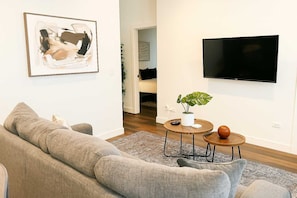 A living room with a grey sofa, a round coffee table with a plant, a TV mounted on the wall, and a door leading to another room. - Stylish 4BR Stay-Prime Location (Chicago)