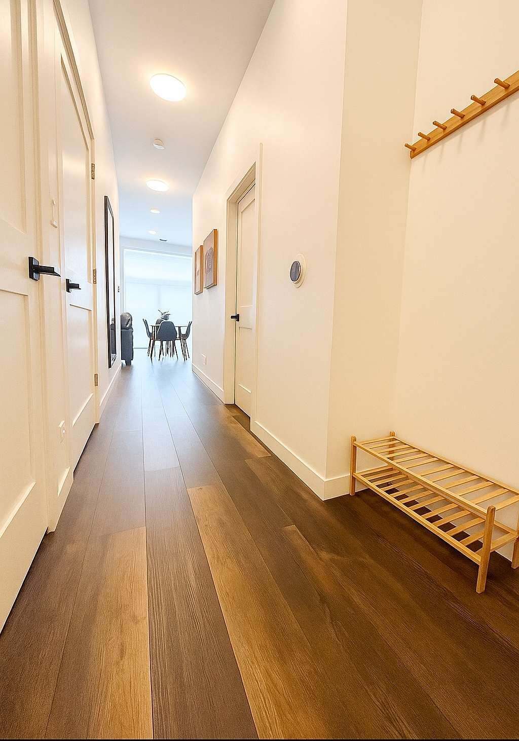 Un couloir doté d’un plancher en bois, de murs blancs et d’un banc en bois.