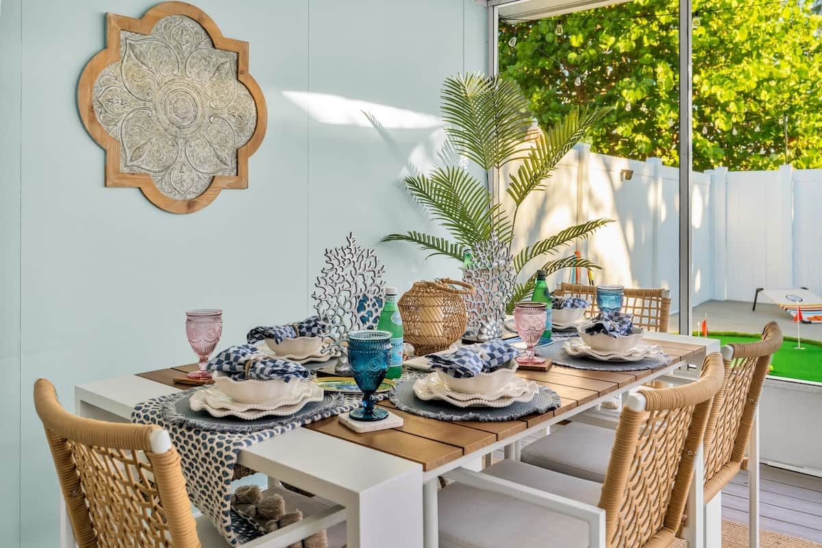 A dining area with a white table set for four, surrounded by wicker chairs.
