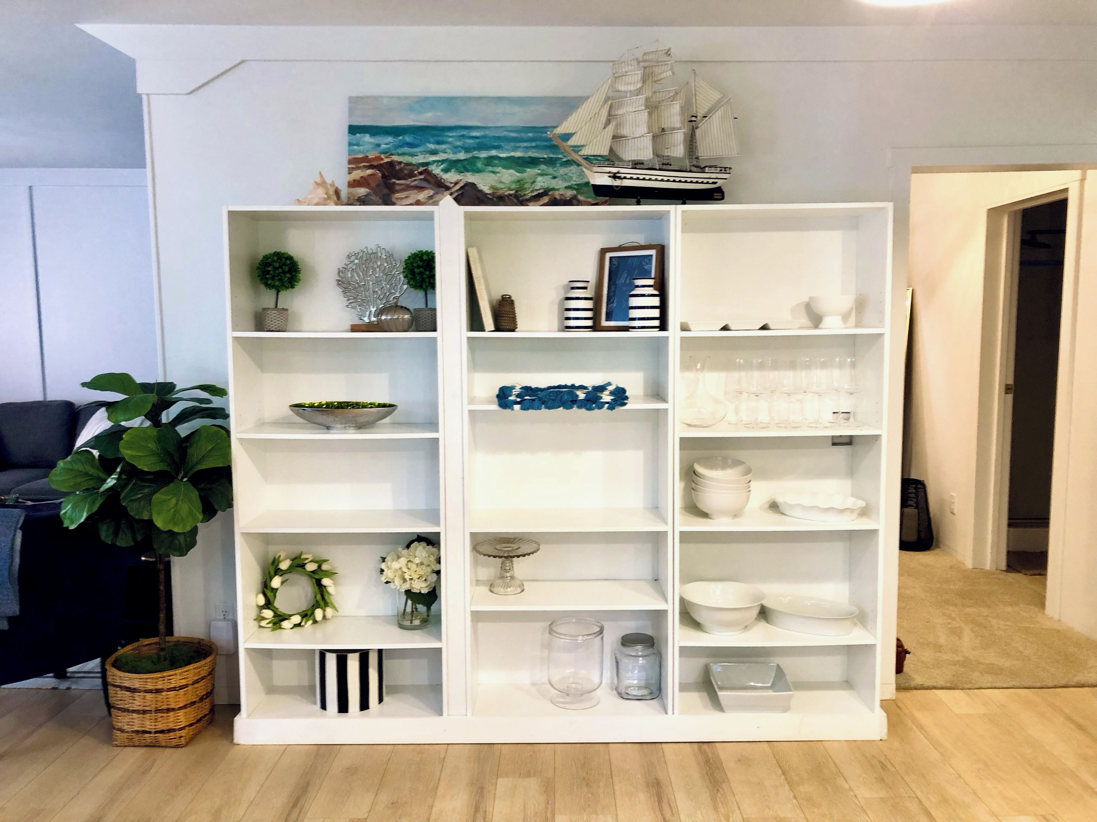 A white shelving unit with decorative items, a ship model, and a potted plant.
