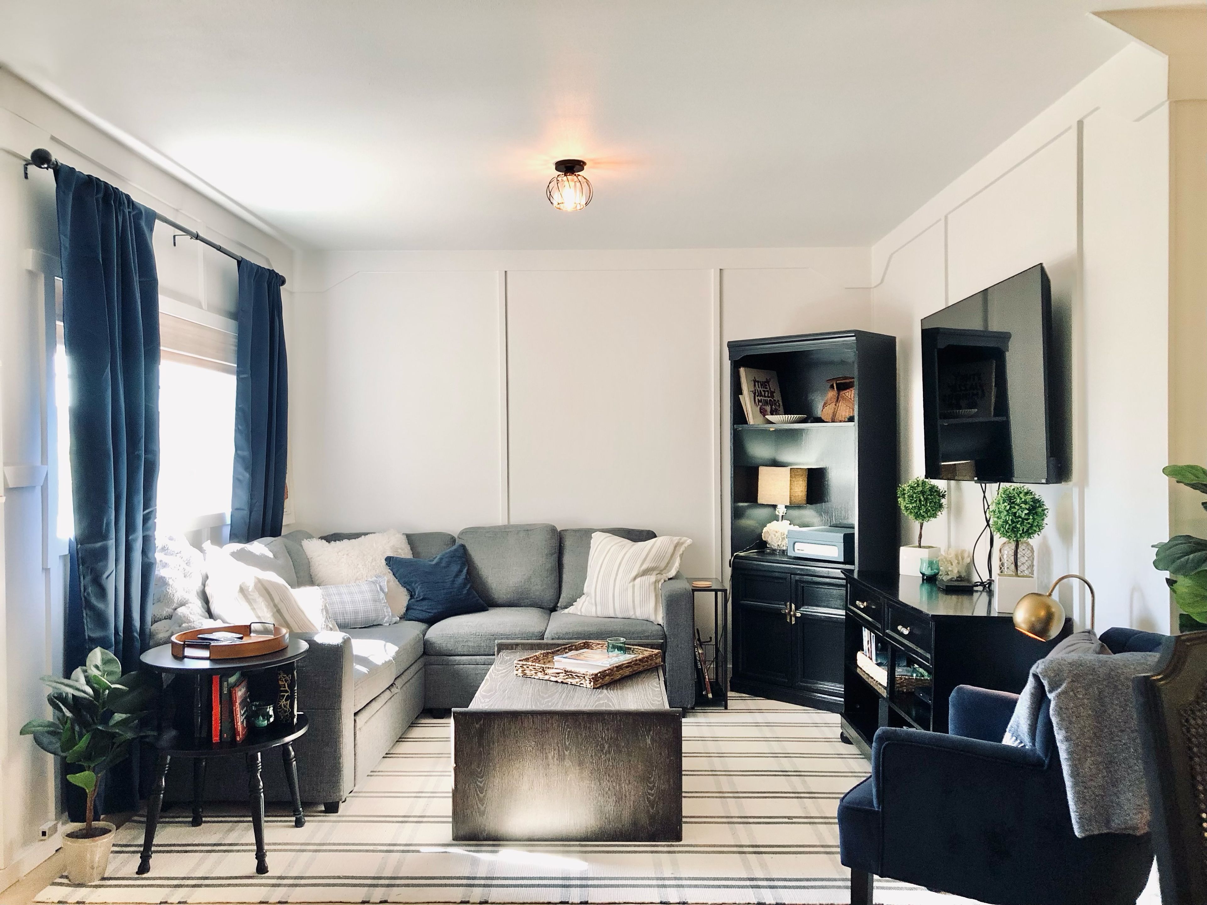 Un salon moderne avec un canapé d’angle, une table basse, un meuble TV noir et un tapis à rayures.