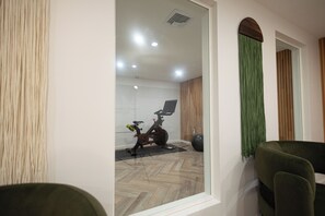 A room with a wooden floor, a black exercise bike, a green curtain, and a dining area with green chairs.