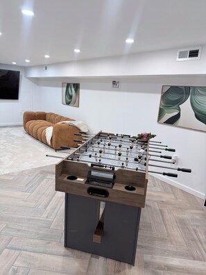 Una habitación moderna con mesa de futbolín, un sofá marrón y obras de arte en las paredes.