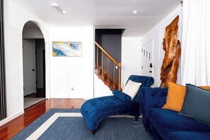 Una sala de estar moderna con un sofá azul, una escalera de madera y un cuadro abstracto grande.