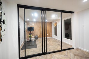 A modern interior with a sliding glass door leading to a room with exercise equipment and a herringbone wood floor.