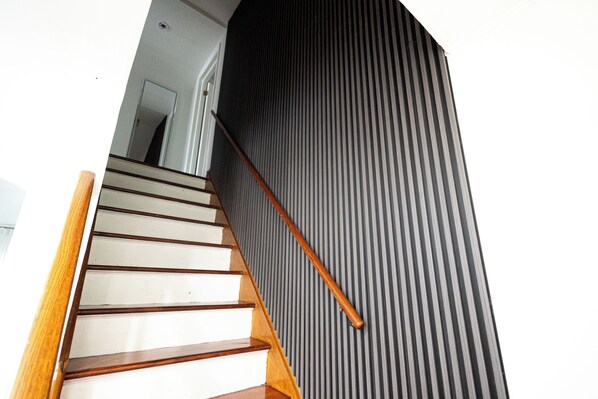 A staircase with wooden steps and a handrail, leading to a room with a dark, ribbed wall.