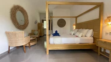 A room with a four-poster bed, a wicker chair, a round mirror, and a wall-mounted light fixture.