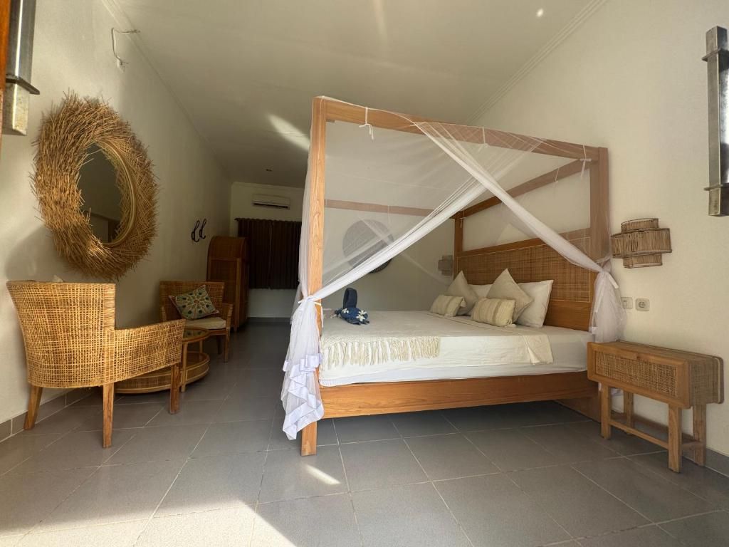 Quarto com cama de dossel, uma cadeira de vime, uma mesinha e um espelho fixado na parede.