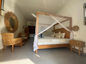 Une chambre à coucher avec un lit à baldaquin, une chaise en osier, une petite table et un miroir fixé au mur.