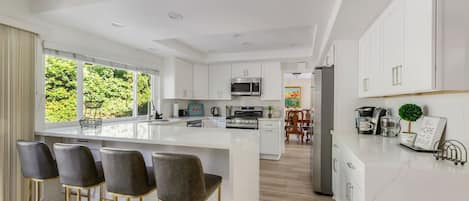 A modern kitchen with a large island, bar stools, and a view of greenery outside.