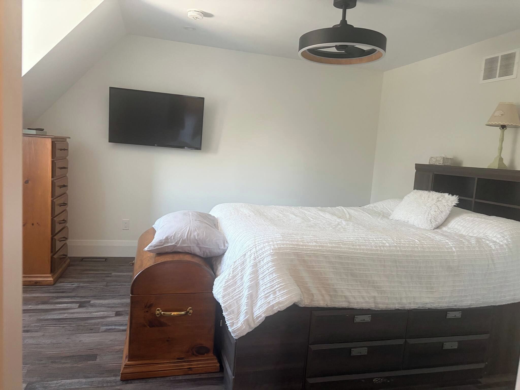 Ein Schlafzimmer mit einem Bett, einem Schminktisch, einem Fernseher und einem Deckenventilator.