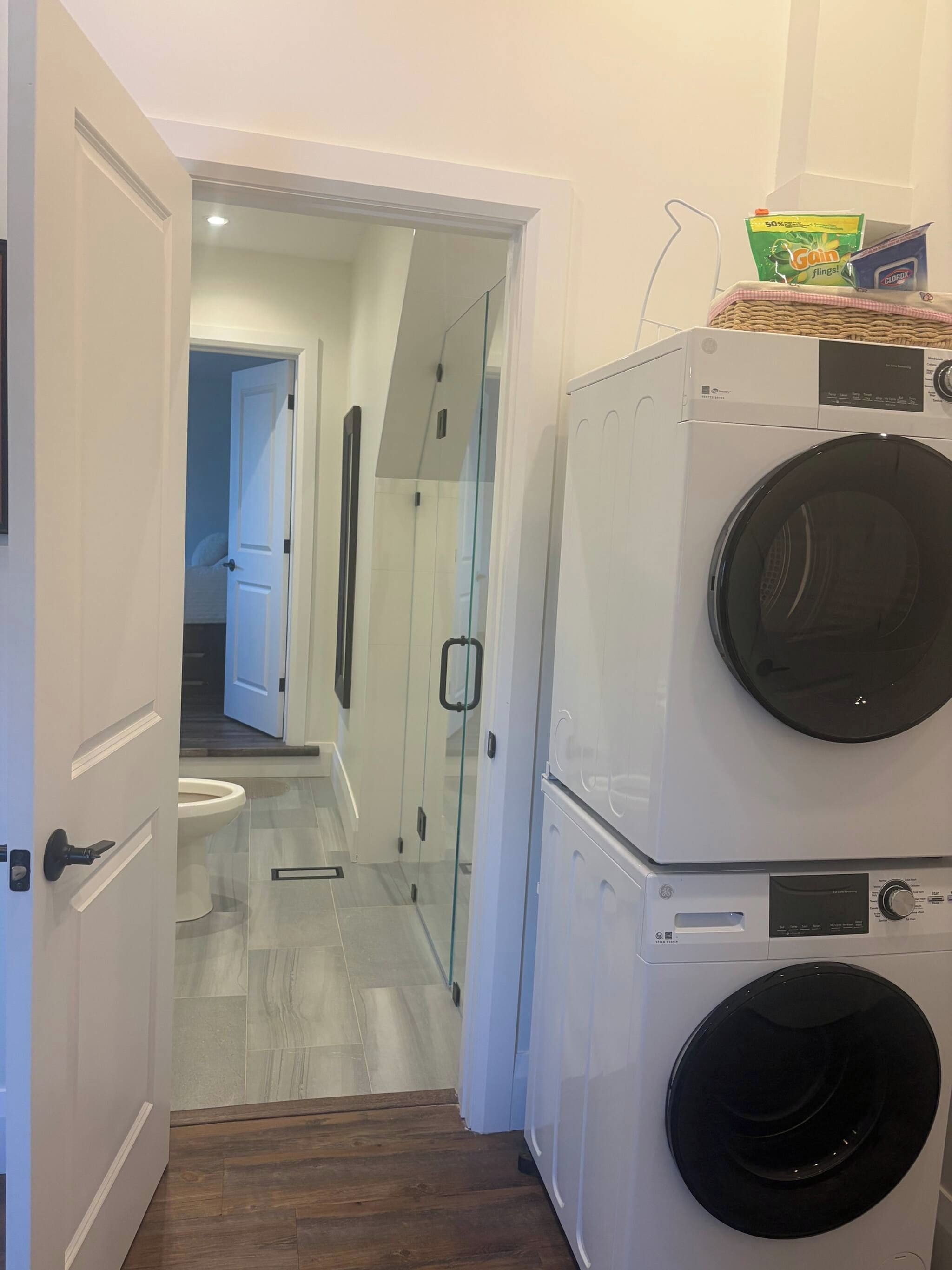 Un espace buanderie avec des machines à laver superposées et une cabine de douche en verre.