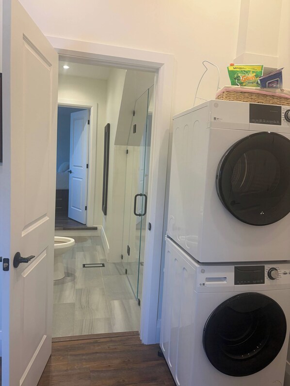A laundry area with stacked washing machines and a glass shower enclosure.