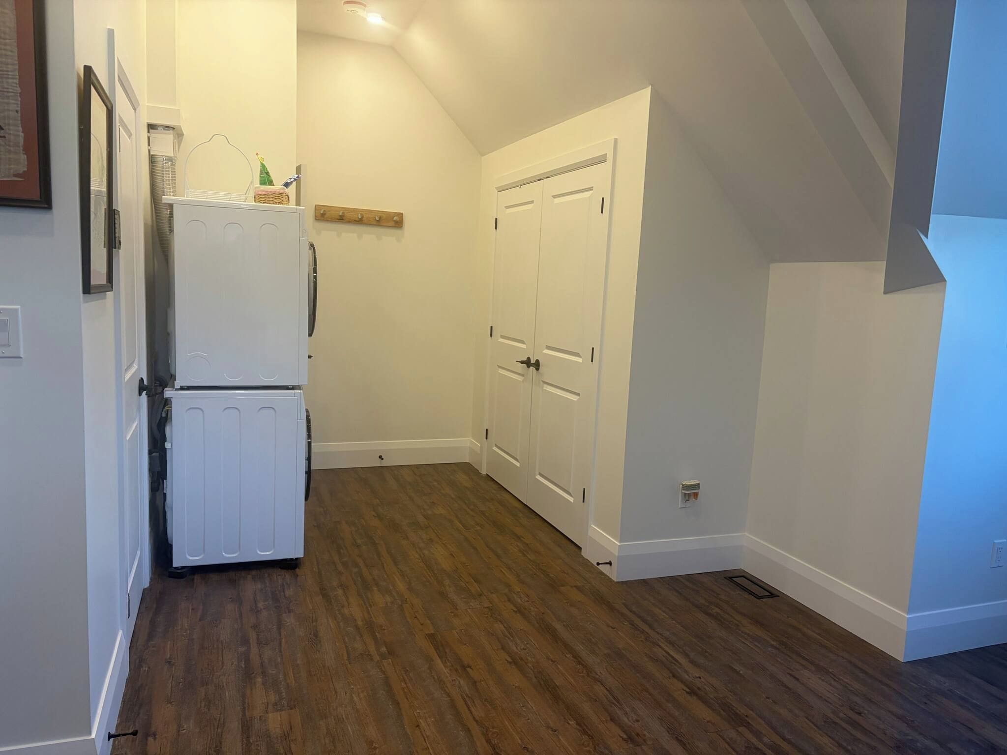 Un pasillo estrecho con suelo de madera, paredes blancas y un refrigerador blanco.