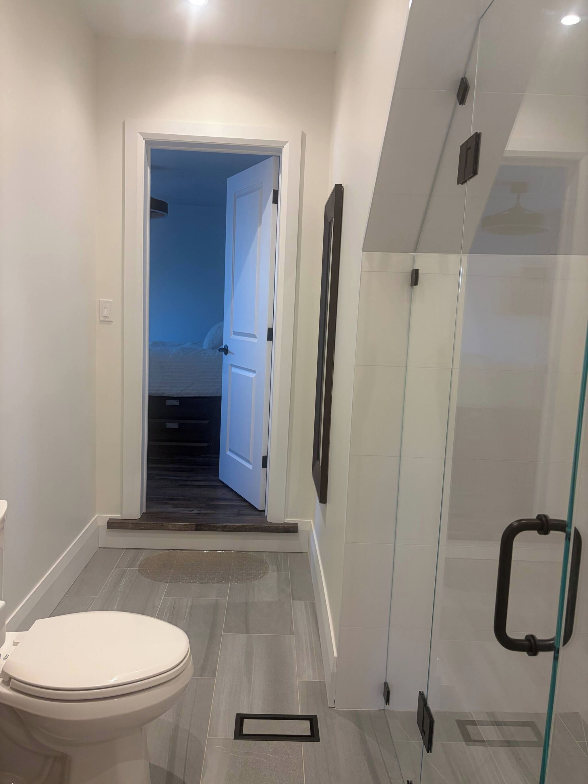 A modern bathroom with a toilet, a shower with a glass door, and a visible staircase leading to another room.